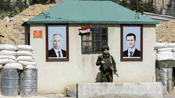 1 март куни олинган суратда Россия ҳарбий полицияси ходими Дамашқ яқинидаги ал-Вафидийн чегара пунктида Сурия президенти Башар ал-Ассад (ўнгда) ва Россия президенти Владимир Путин (чапда) портретлари ўртасида қўриқчилик постида тургани акс этган. (Louai Beshara/AFP)